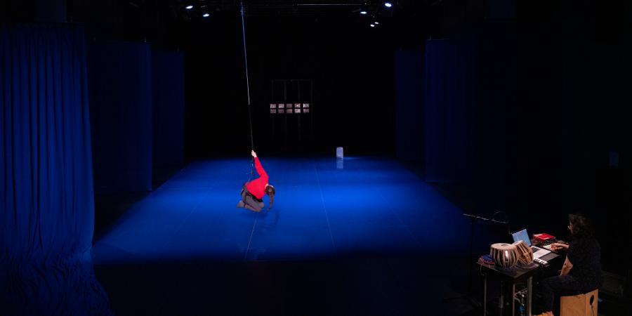Eine Person mit einem roten Pullover hängt am Ende eines Seils, das von der Decke fällt