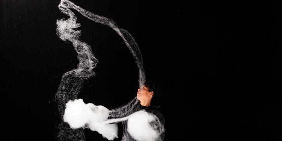 Eine Frau, schwarz gekleidet vor einem schwarzen Hintergrund, spielt mit Zuckerwatte