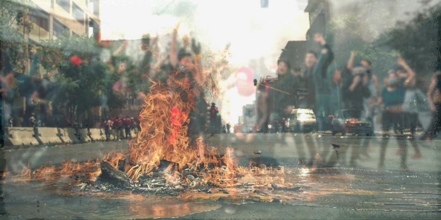 Brennender Rest eines Autos, im Hintergrund jubelnde Menschen